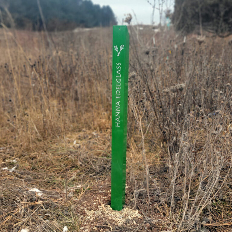 a green metal post in a field with a name painted on it in white