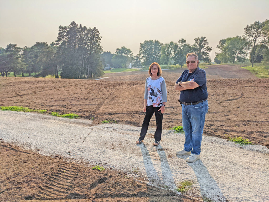 A man and woman stand in an open field on a gravel path.