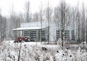 A winter scene of a building in the woods with a utility vehicle in front of it.