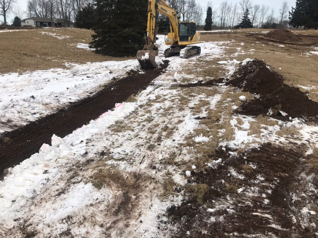 clear dirt path in snowy field with excavation vehicles in background