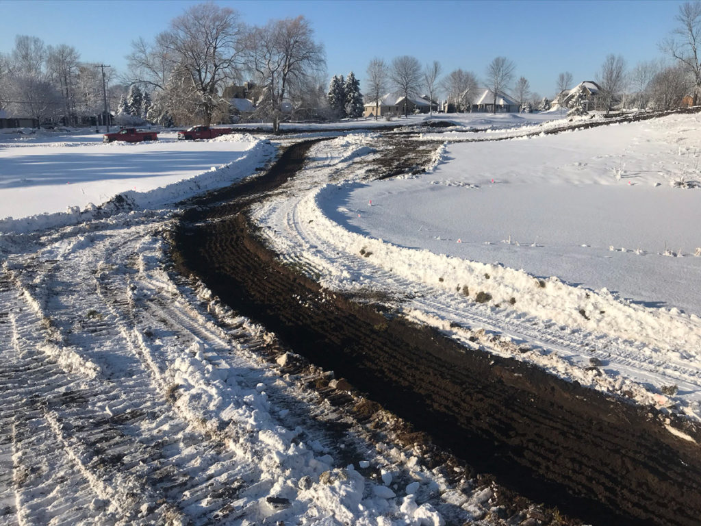 clear dirt path in snowy field with a row of homes in background