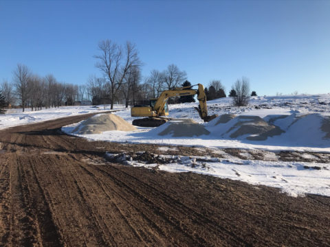 clear dirt path in snowy field with excavation vehicles in background