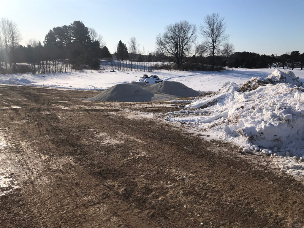 fresh brown dirt in a snowy field with a pile of gravel