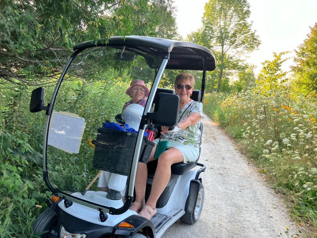 Two women laughing in a modified golf cart on a trail.