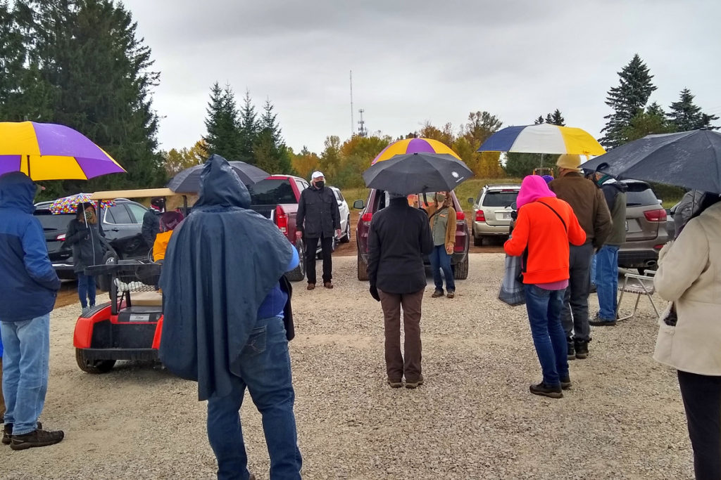 a gravel parking lots with a dozen people holding umbrellas and dressed warmly.