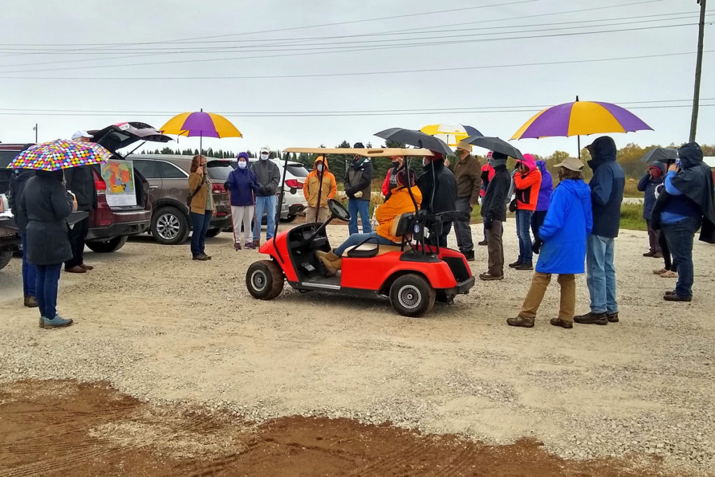 a gravel parking lots with a dozen people holding umbrellas and dressed warmly.