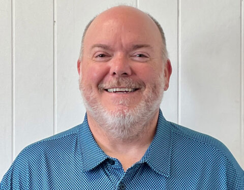 a middle-aged Caucasian man with a gray beard and a bright blue polo shirt.