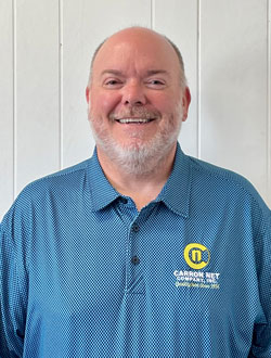 A middle-aged Caucasian man with a gray beard and a bright blue polo shirt with a yellow logo that says Carron Net.