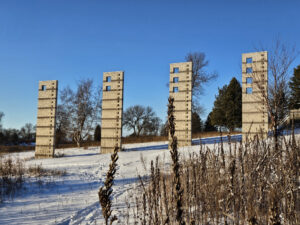 4 large concrete monoliths on a bed of snow with trees in the background.