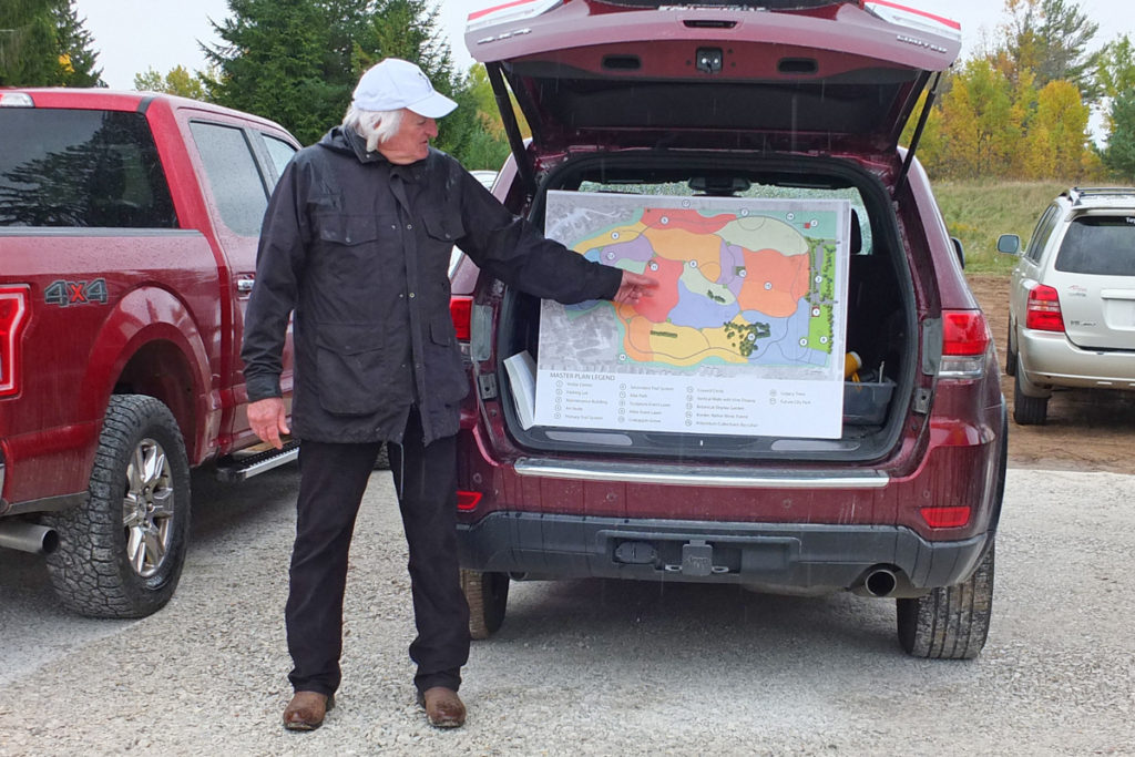 A large poster of a map in the back of a red SUV, which is open. A man stands and points to something on the map.