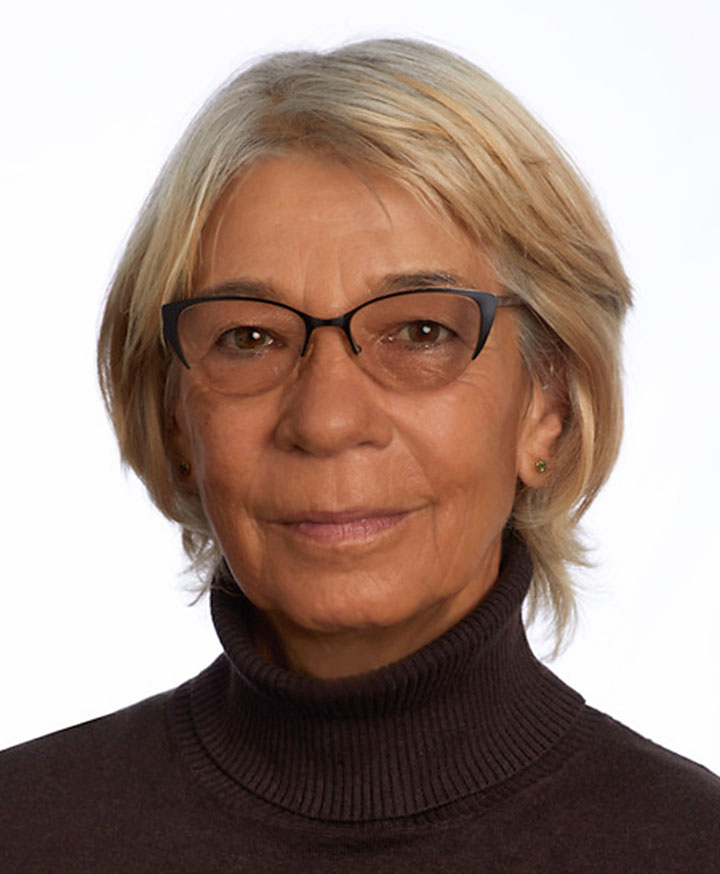 an older caucasian female with short blonde hair, tan skin, lasses, and a black turtleneck