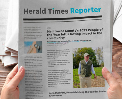 hands holding a newspaper with the title Herald Times Reporter and a photo of John Durbrow