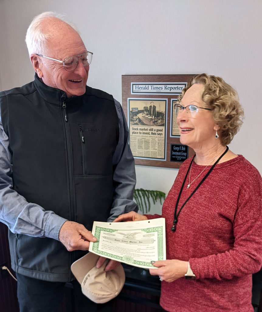 a smiling man and woman exchange a stock certificate in an office setting