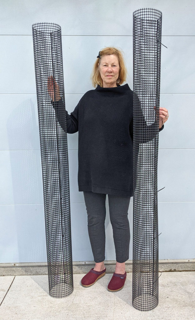 a woman stands holding two tree guards