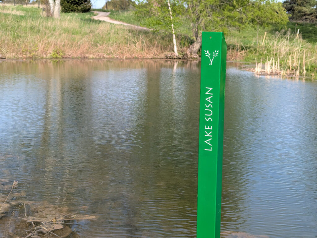 a green metal stake at the edge of a pond with the words LAKE SUSAN and the VDBA logo